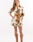 Woman wearing a floral dress with a tie waist and brown boots on a white background