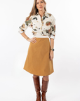 Woman wearing a floral blouse and mustard skirt with brown knee-high boots on a white background
