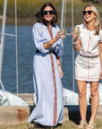Two women standing by a body of water, holding drinks and smiling.