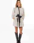 Woman wearing a patterned dress with a black belt and black boots on a white background