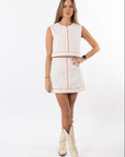 Woman wearing a white dress with red accents and cream cowboy boots on a white background