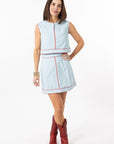 Woman wearing a light blue checkered dress with red accents and red cowboy boots on a white background