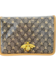 A Gucci shoulder bag in GG Supreme canvas with a glossy finish, featuring a gold-tone bee charm on the front and a tan leather trim.