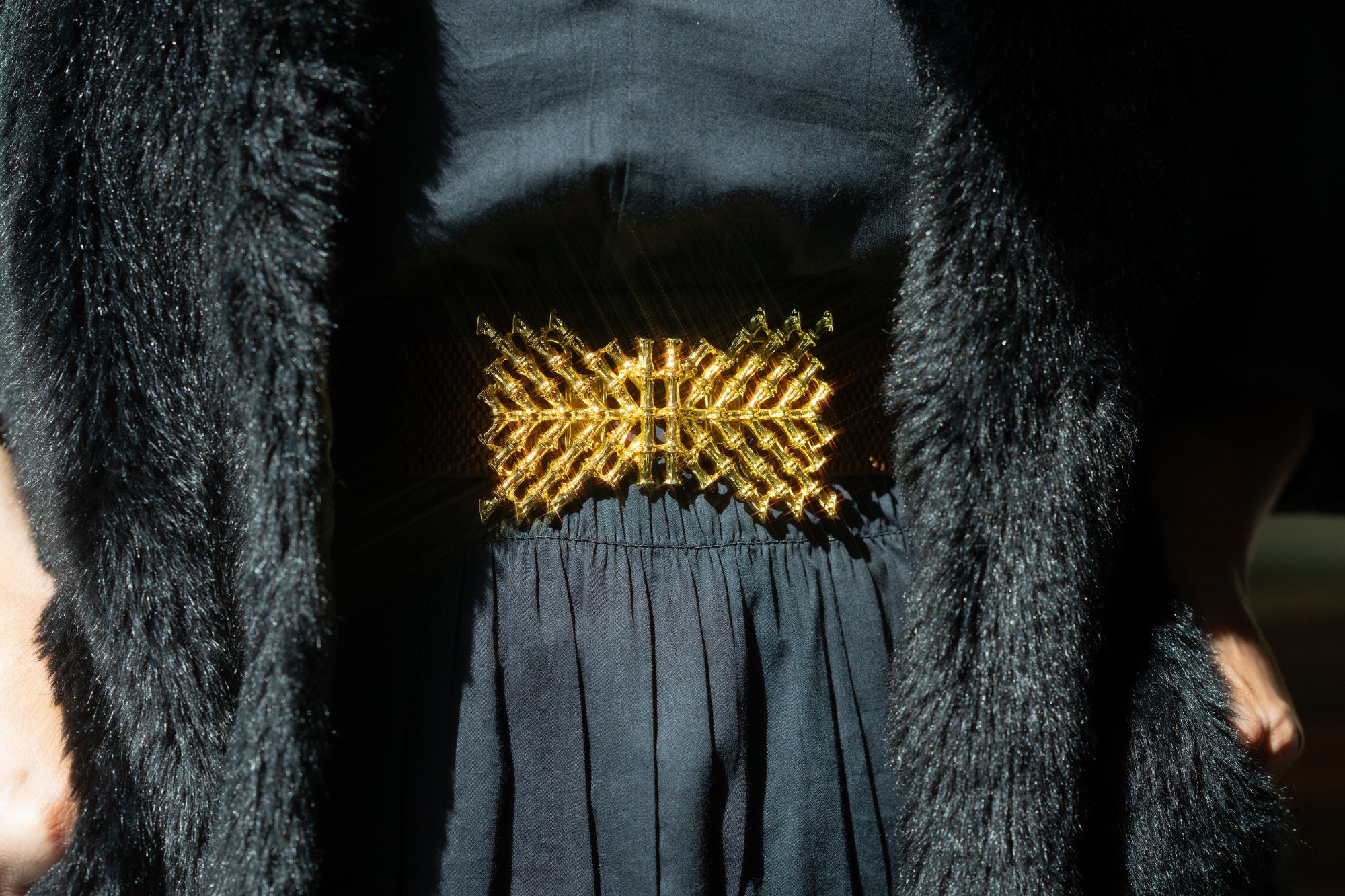 Person wearing a black dress with a gold belt and a textured black coat.