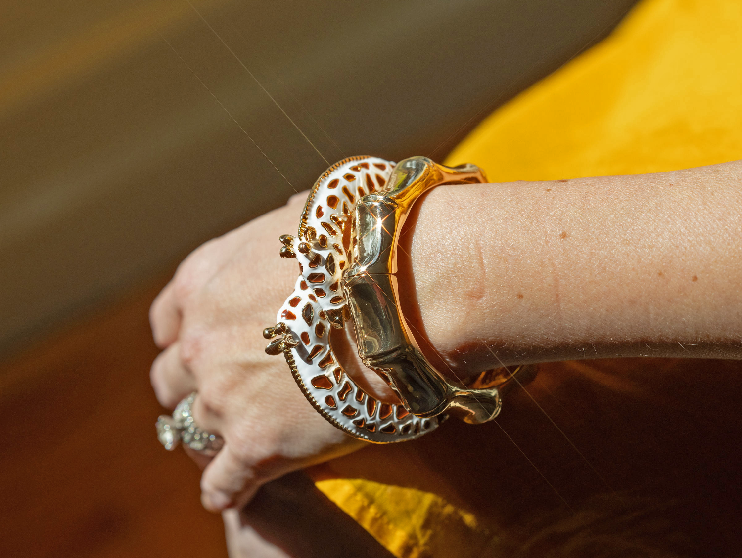 Close-up of a wrist wearing a gold bracelet with intricate designs, against a blurred background.