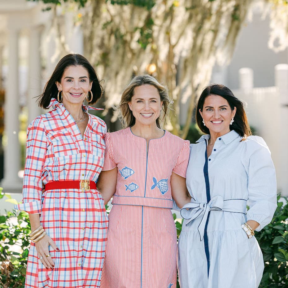 Three women standing outdoors wearing colorful garland dresses 