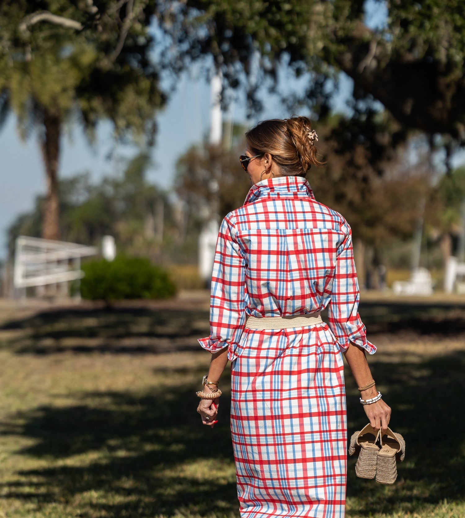 Woman in a red, white, and blue checkered dress walking outdoors.