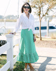 Woman in a white blouse and green skirt standing by a waterfront.